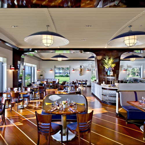 Elegantes Meeresfrüchterestaurant mit Holzboden, großen Fenstern und modernen Lichtinstallationen, mit Tischen zum Essen.