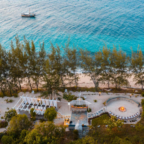 Eine Luftaufnahme einer abgelegenen Insel mit Strand, umgeben von Bäumen und einigen Booten im klaren blauen Meer.