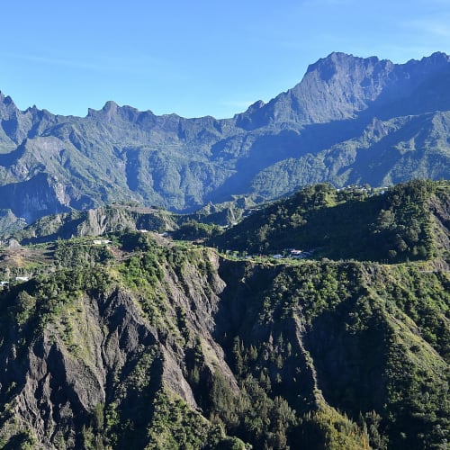 Panoramablick auf die gebirgige Landschaft von Cilaos mit üppiger grüner Vegetation unter klarem blauem Himmel.