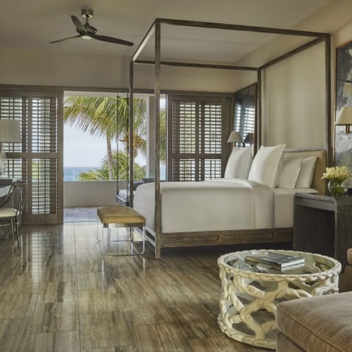 Luxuriöses Hotelzimmer mit einem Himmelbett und einem Balkonblick auf Palmen und das Meer.