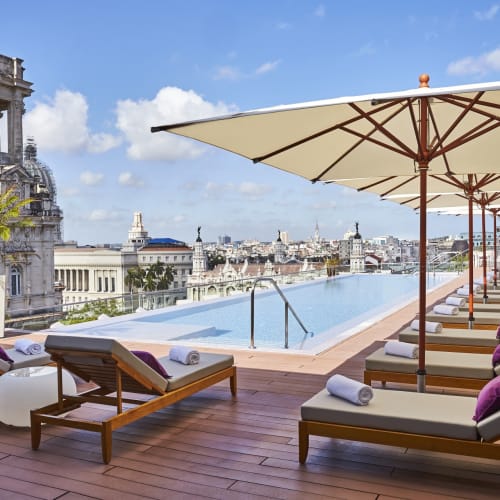 Luxuriöse Dachpool-Atmosphäre mit Liegestühlen und Sonnenschirmen mit Blick auf die historische Altstadt von Havanna