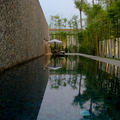 Ein ruhiger Swimmingpool mit dunklen Fliesen, die den Himmel und die umliegende Vegetation widerspiegeln, in einer ruhigen Resort-Umgebung.
