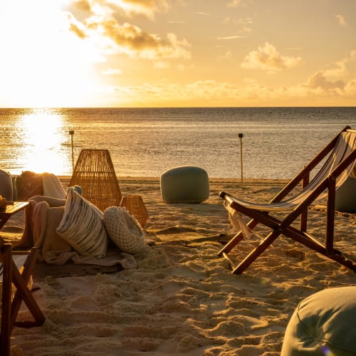 Strandstühle und Kissen am Sandstrand bei Sonnenuntergang am Meer, mit weichem goldenem Licht und ruhigem Meer.
