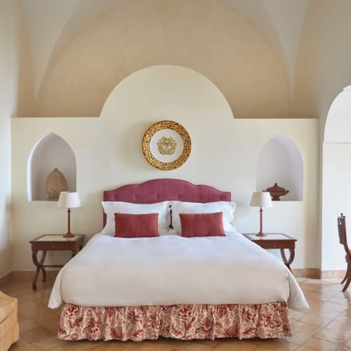 Elegant bedroom with a large bed, red accents, and decorative niches in a luxurious hotel suite in Amalfi.