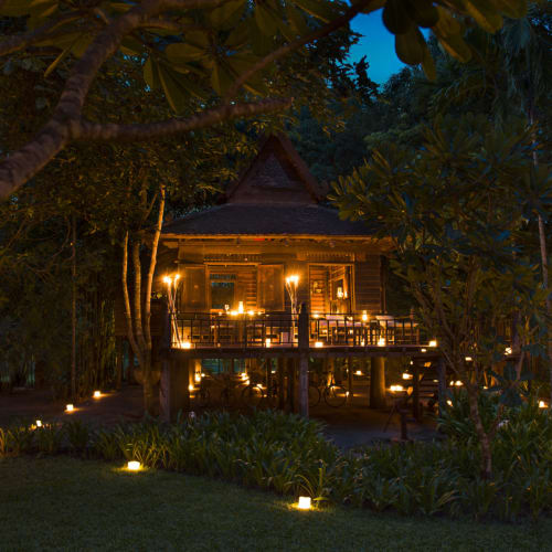 Eine schön beleuchtete zweistöckige Khmer-typische Villa, umgeben von Bäumen bei Nacht, mit Weglichtern, die den Garten erhellen.