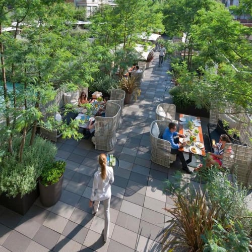 Terrasse im Freien im Mandarin Oriental Barcelona mit üppigem Grün und Menschen, die an Tischen speisen.