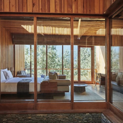 Ein luxuriöses Schlafzimmer mit Holzvertäfelung und großen Glastüren, die zu einem Balkon mit Blick auf Bäume und Himmel führen.