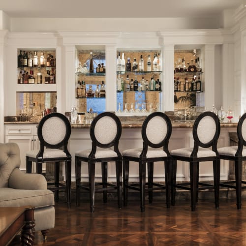 Eine luxuriöse Bar mit fünf hohen Stühlen vor einem gut bestückten Spirituosenregal hinter einer weißen Holztheke.