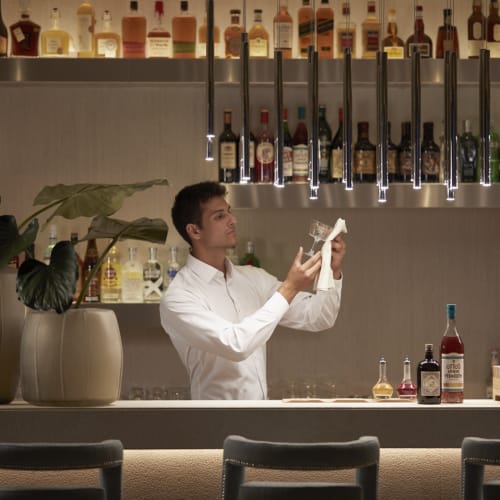 Ein Barkeeper bereitet einen Cocktail hinter einer Bar mit Flaschen an der Wand vor.