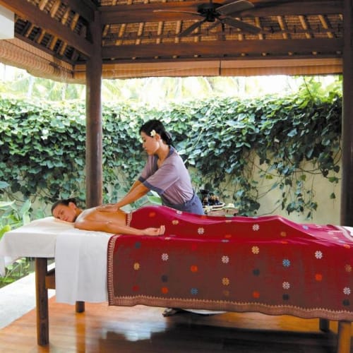 Eine Person erhält eine Massage an einem Massagebett im Freien unter einem Pavilon, umgeben von grünen Pflanzen.
