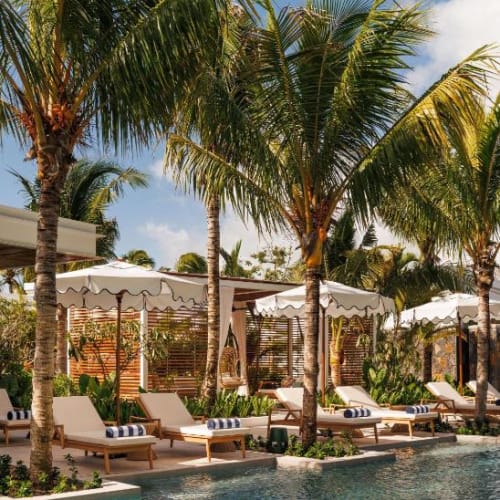 Luxuriöse Poolseite mit Sonnenliegen und weißen Sonnenschirmen, umgeben von Palmen.