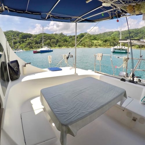 View from the cockpit of a sailboat with a covered storage area, overlooking calm water with other boats and lush green hills.