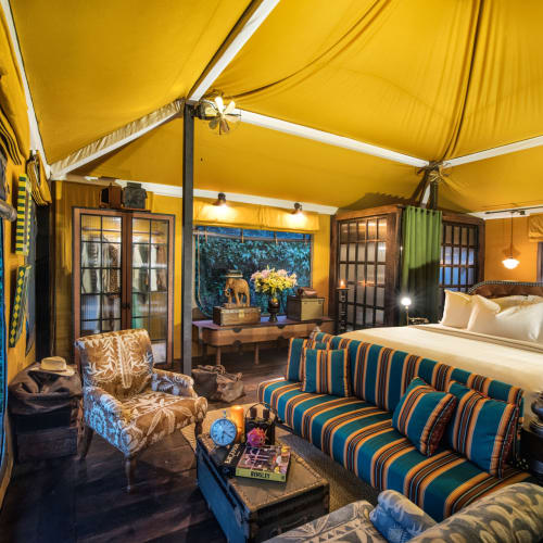 Luxury interior of a tent accommodation with a large bed, striped sofa, and decorative furniture inside a spacious tent with yellow fabric and large windows.