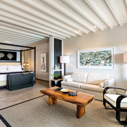 Geräumige Hotellsuite mit einem Wohnbereich, einem Himmelbett im Schlafzimmer und modernen Möbeln in einem hellen Raum mit Holzakzenten.