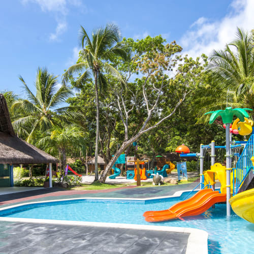 Colorful water slides and play structures in a children's pool surrounded by palm trees at Tivoli Eco Resort in Brazil.