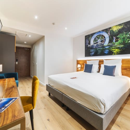 Modernes Hotelzimmer mit Doppelbett, Holztisch mit Stuhl, großem an der Wand montiertem Fernseher und farbenfroher Kunst über dem Bett.