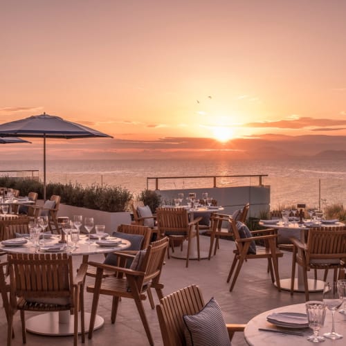 Elegant restaurant terrace overlooking the sea during sunset with tables set for dining.