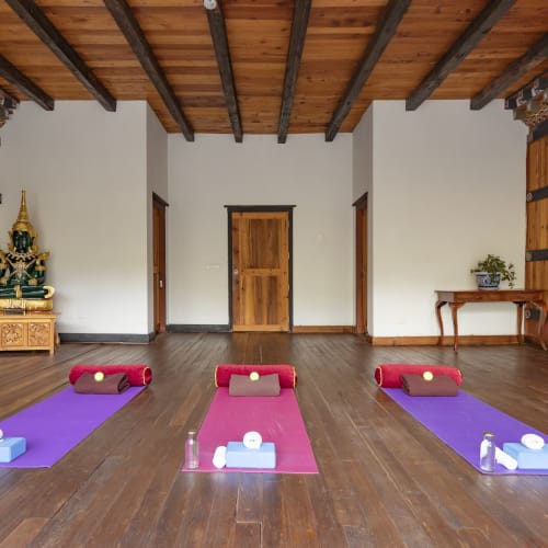 A spacious yoga room with three mats set up in front of a traditional wooden wall, with an altar in the corner.