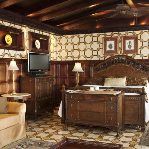 Luxurious hotel room with antique wooden furniture, patterned wallpaper, and a cozy seating area.