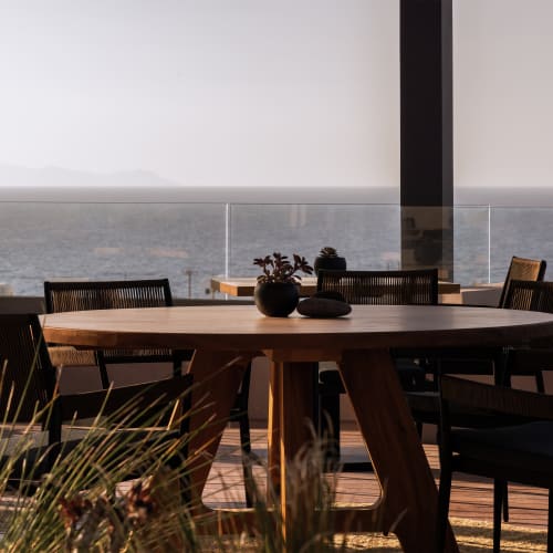 Ein Dachterrassen-Essbereich mit einem runden Holztisch, umgeben von schwarzen Stühlen, mit Blick auf eine neblige Stadtsilhouette und entfernte Berge unter hellem Himmel.