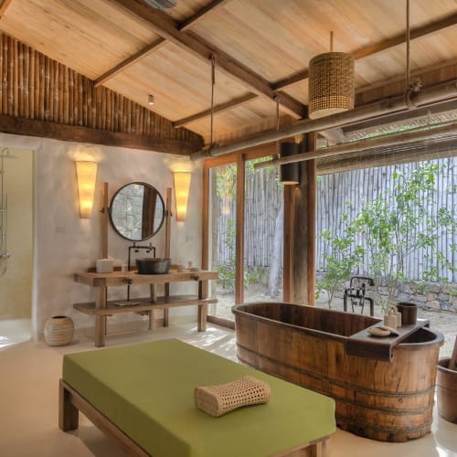 A luxurious bathroom with a wooden bathtub near large glass doors overlooking a garden.