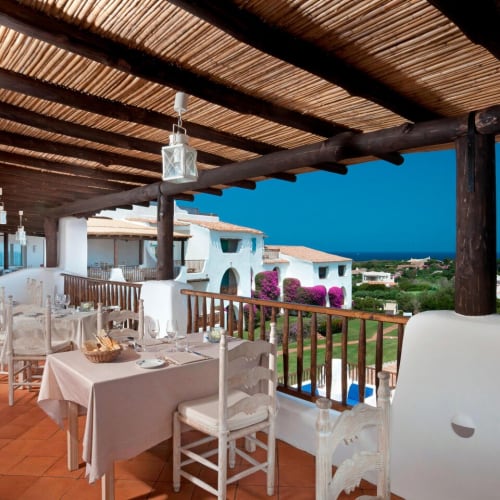 A spacious outdoor restaurant terrace with white tables and chairs, overlooking a scenic view of rooftops and greenery at dusk.