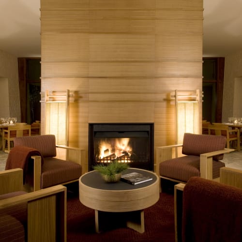 Cozy living room with a fireplace surrounded by comfortable chairs and warm lighting in a rustic setting.