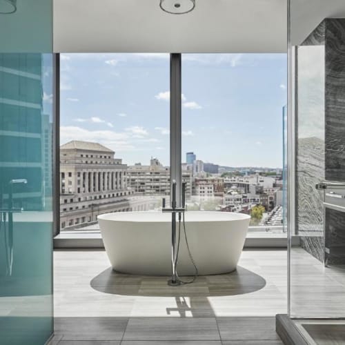 A luxurious modern bathroom with a standalone bathtub facing large floor-to-ceiling windows offering a city view.