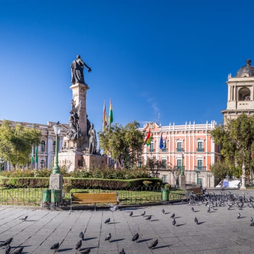 Historischer Platz mit Statue und kolonialstiligen Gebäuden, Tauben auf dem Boden unter einem klaren blauen Himmel.