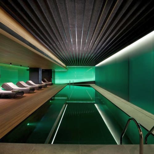 Luxuriöses Hallenbad mit modernem Design, mit grüner Beleuchtung und Sonnenliegen entlang des Holzdecks.