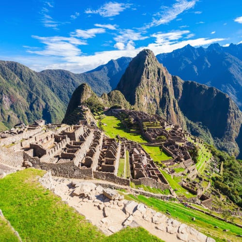 Antike Inka-Ruinen von Machu Picchu mit grünen Terrassen und bergigem Hintergrund unter einem blauen Himmel.