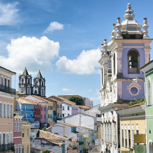 Bunte koloniale Gebäude und eine Kirche mit einem Glockenturm in Salvador da Bahia unter einem blauen Himmel mit Wolken.