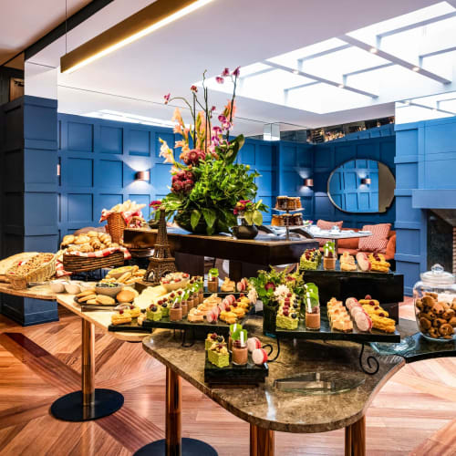 Ein luxuriöses Buffet in einem stilvollen Hotel mit einer lebendigen Blumenarrangement in der Mitte, das Desserts und Snacks auf eleganten Tischen und Theken präsentiert.