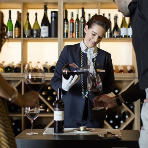 Eine Frau in Uniform serviert Wein an zwei Gäste in einem gemütlichen Weinkeller eines Boutique-Hotels.
