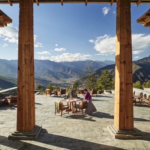 Aussicht auf die Terrasse des Six-Senses Paro mit Bergen im Hintergrund und Menschen, die an Tischen sitzen.