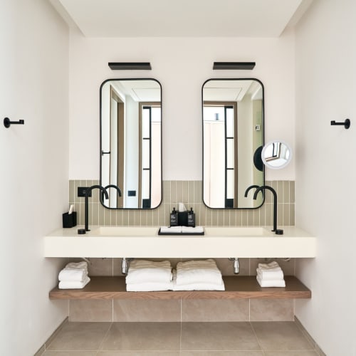 Modernes Badezimmer mit Doppelwaschtisch, zwei Spiegeln, schwarzen Armaturen und ordentlich gefalteten Handtüchern unter dem Waschbecken.