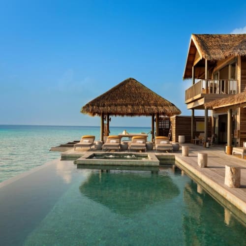 Luxusvilla mit einem Pool am Rande des Ozeans, mit einer Hütte mit Strohdach und Liegestühlen.