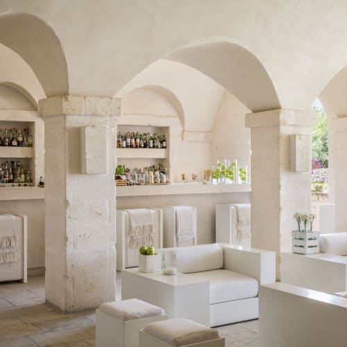 A bright, white interior of a bar with arched ceilings, white sofas, and a well-stocked bar shelf.