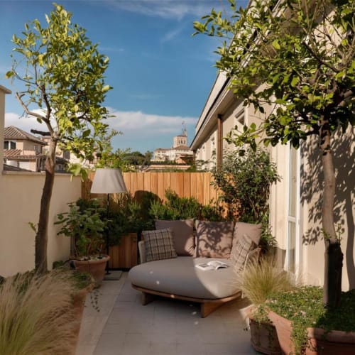 A cozy outdoor terrace with a round sofa, potted trees, and lush plants under a bright blue sky in Rome.