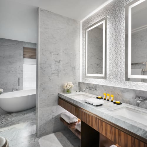 Luxurious bathroom with a marble vanity, illuminated mirrors, and a freestanding bathtub overlooking a window.