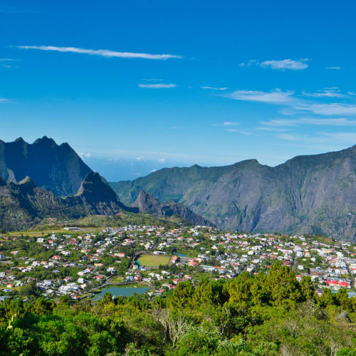 Panoramablick auf eine kleine Stadt in einem üppig grünen Tal, umgeben von steilen, felsigen Bergen unter klarem blauem Himmel.