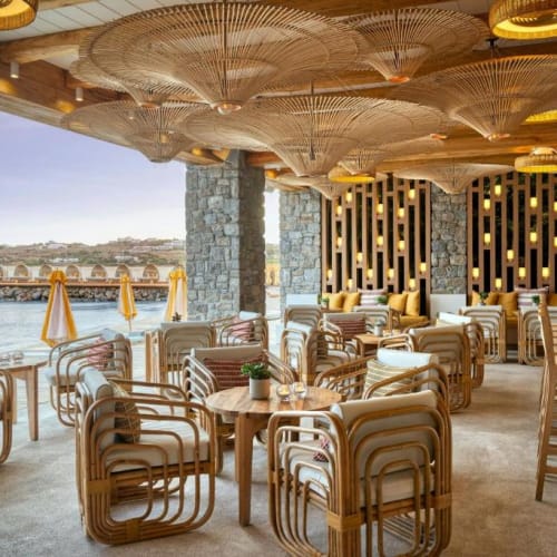 Elegante Open-Air-Bar mit Holzmöbeln und Blick auf das Meer, dekoriert mit modernen und rustikalen Elementen, in einem Luxushotel.