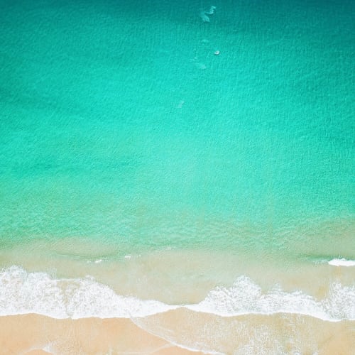 Aerial view of a beach with turquoise waters and gentle waves hitting the sandy shore.