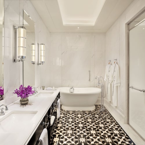 Luxurious bathroom with a freestanding bathtub, double sink vanity with purple flowers, and elegant white walls.
