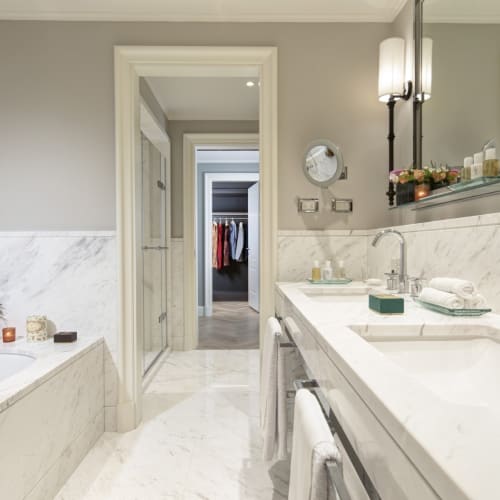 Luxuriöses Hotelbadezimmer mit Marmor-Arbeitsplatten, Doppelwaschbecken, großem Spiegel und eleganter Dekoration, einschließlich Blumen und Kerzen.