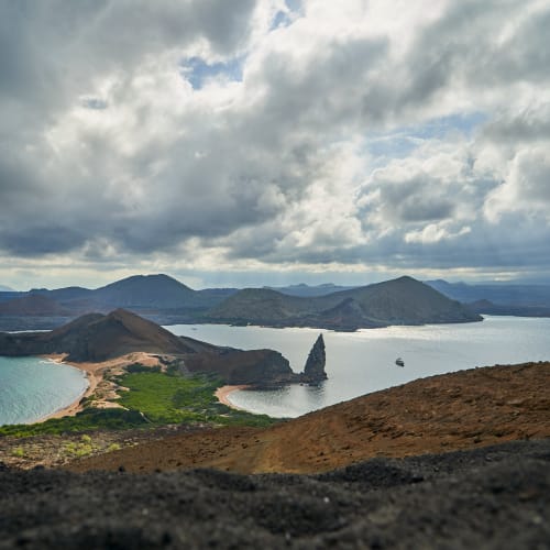Eine malerische Aussicht auf die vulkanische Insel mit grünem und felsigem Terrain, einem Sandstrand und den umliegenden blauen Gewässern unter bewölktem Himmel.