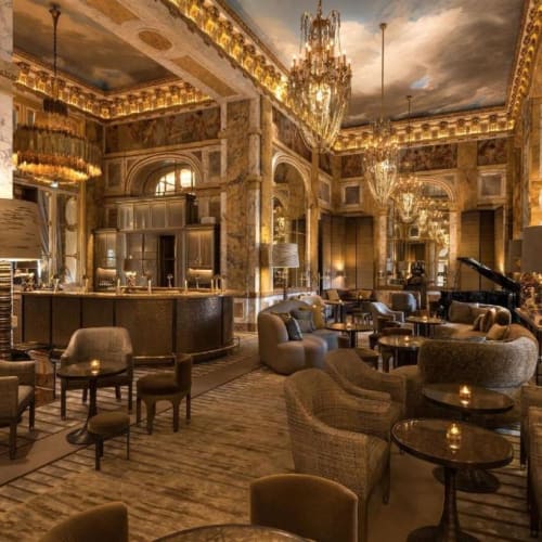 Elegantes Hotel-Lounge mit Kristall-Kronleuchtern, exotischen Marmorwänden und gemütlichen Sitzgruppen mit Tischen.