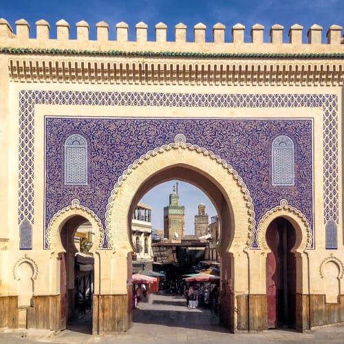Colorful historic city gate with intricate tile work and a view of city buildings through the arch.
