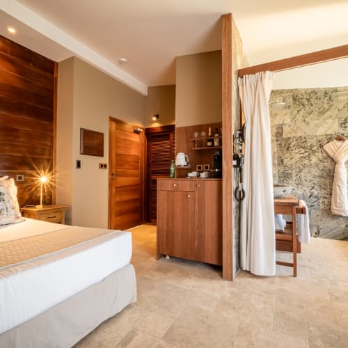 Geräumiges modernes Schlafzimmer mit angrenzendem Bad, großem Bett, Holzakzenten, Steinwand und zu dekorativen Formen gefalteten Handtüchern.