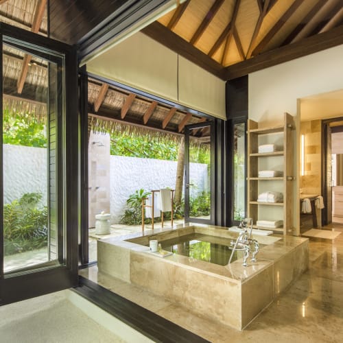 Eine geräumige Strand-Suite mit einer großen Badewanne vor Glas Türen, die auf einen üppigen Garten und Strandblick öffnen.